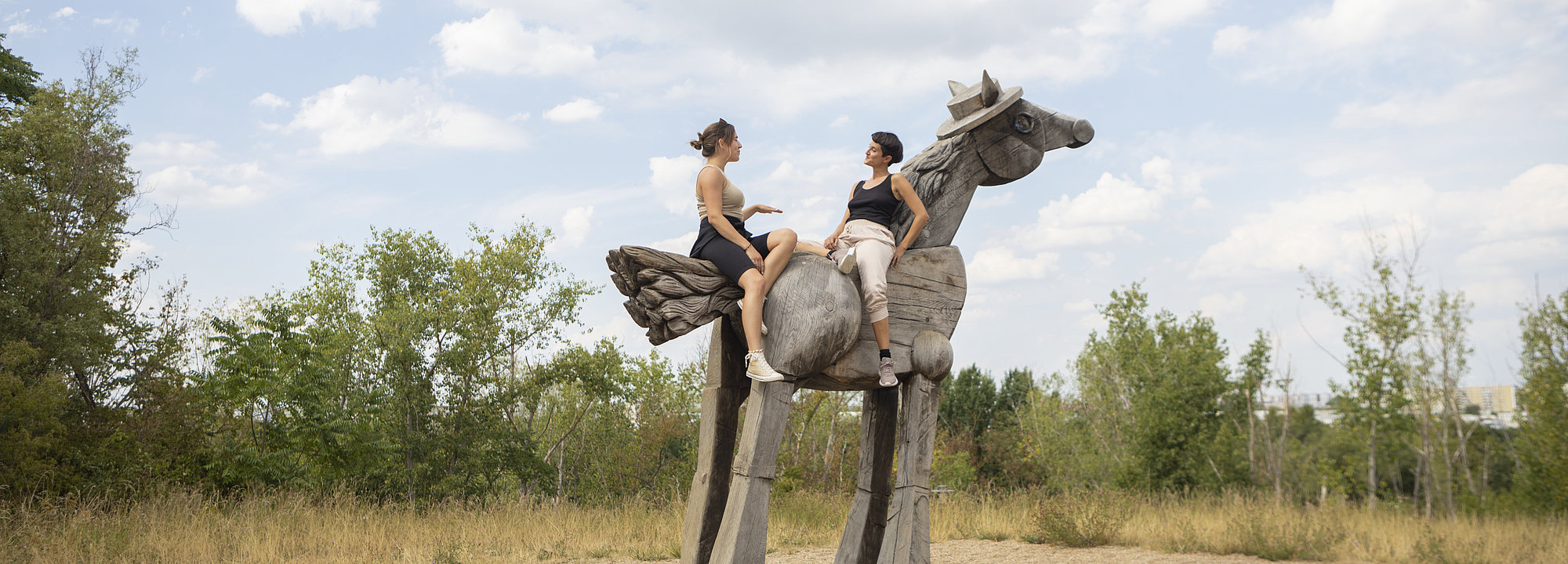 Zwei Frauen sitzen auf dem Caballo Negro, einem Holzpferd im Kienbergpark